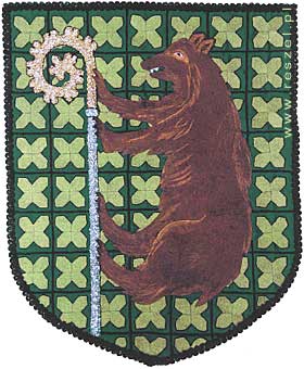 Herb Gminy Reszel<br />
Wizerunek niedźwiedzia barwy brunatnej wspinajacego się na laskę biskupią barwy srebrnej ze złotą głowicą.<br />
Tło ciemnozielone z czarnym okratowaniem, w okratowaniu stylizowane motywy żołędzi w kolorze jasnozielonym fot. reszel pl