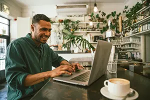 Mężczyzna pracujący zdalnie na laptopie w kawiarni
